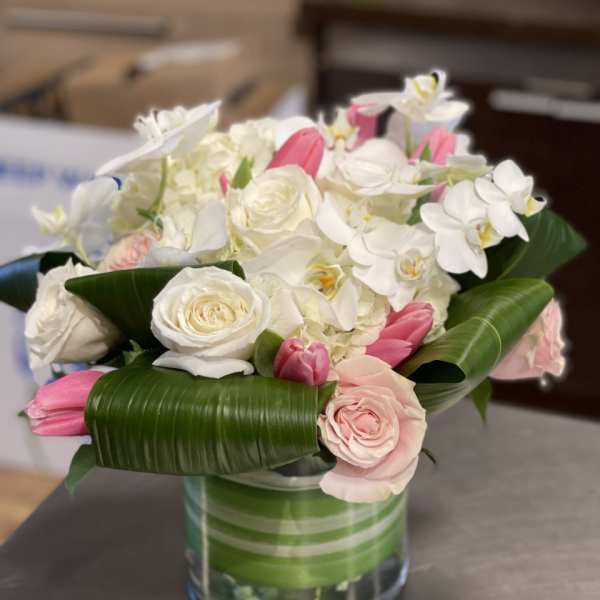 White and pink bouquet in a glass vase with broad green leaves