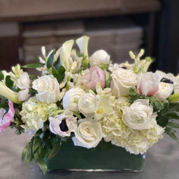 White floral arrangement with roses, ranunculus, and calla lilies in a green vase