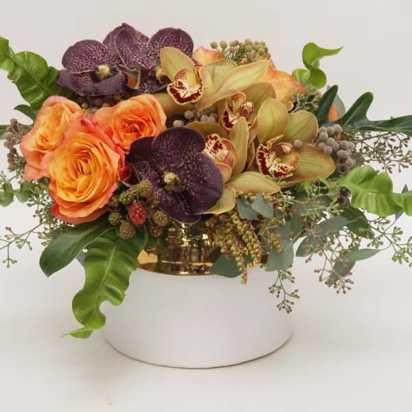 Orange roses and orchids arranged in a gold container