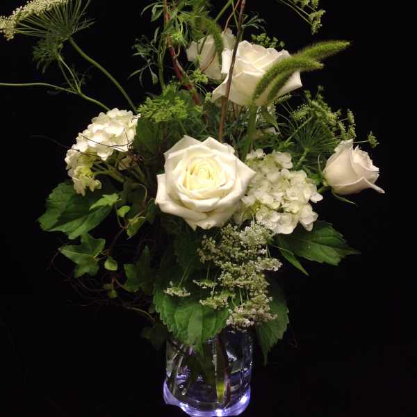 Tall arrangement of white roses and hydrangeas with airy filler in a clear glass vase