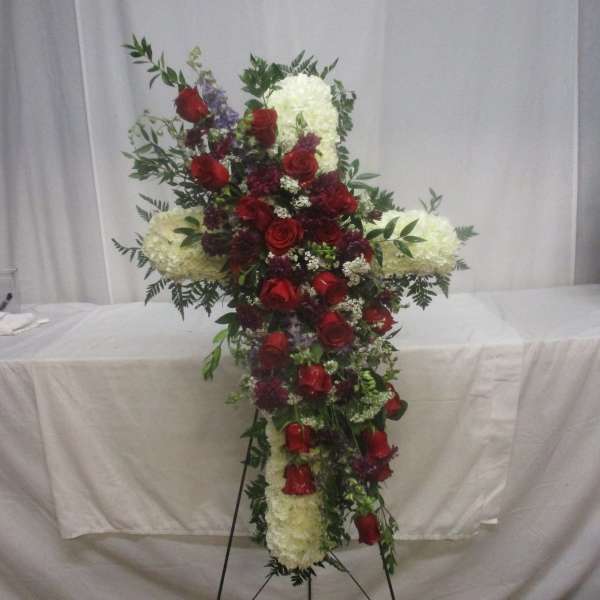 Cross-shaped floral arrangement with red roses and white blooms on a stand