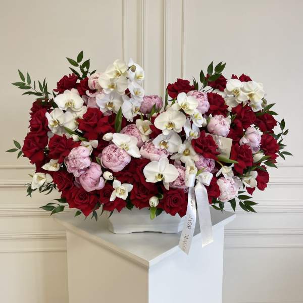 Large arrangement of red roses, pink peonies, and white orchids in a white vase