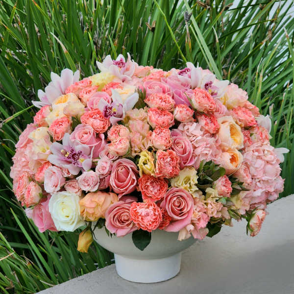 Large pink and peach floral arrangement in a white pedestal vase