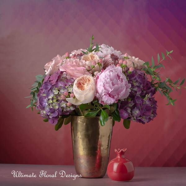 Pink and purple floral arrangement in a gold vase with a small red decorative object