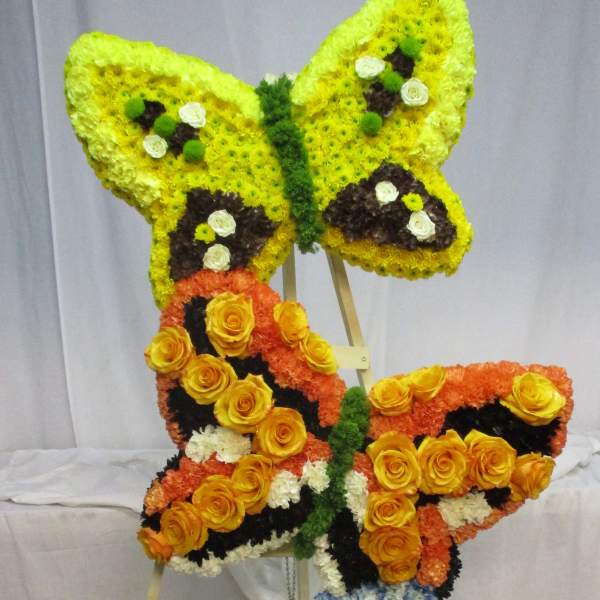 Butterfly-shaped floral display on an easel in yellow, orange, blue, and white.