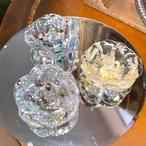 Three glittery glass rose-shaped ornaments on a mirrored tray