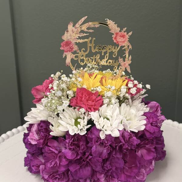 Birthday flower arrangement with a gold topper and purple, white, and yellow blooms