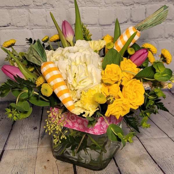 Yellow and white floral arrangement in a glass vase with striped carrot decorations