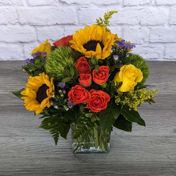 Bouquet of sunflowers, red and yellow roses in a glass vase