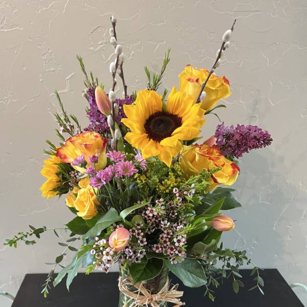 Bouquet of sunflowers, yellow roses, and purple flowers in a glass vase