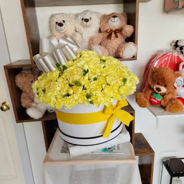 Yellow carnation arrangement in a white hat box with ribbon and bow