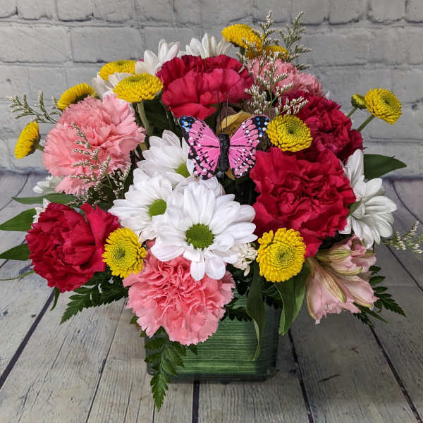 Mixed bouquet of carnations and daisies in a green vase with a butterfly pick