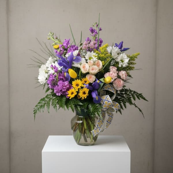 Mixed bouquet of purple, white, pink, and yellow flowers in a glass vase