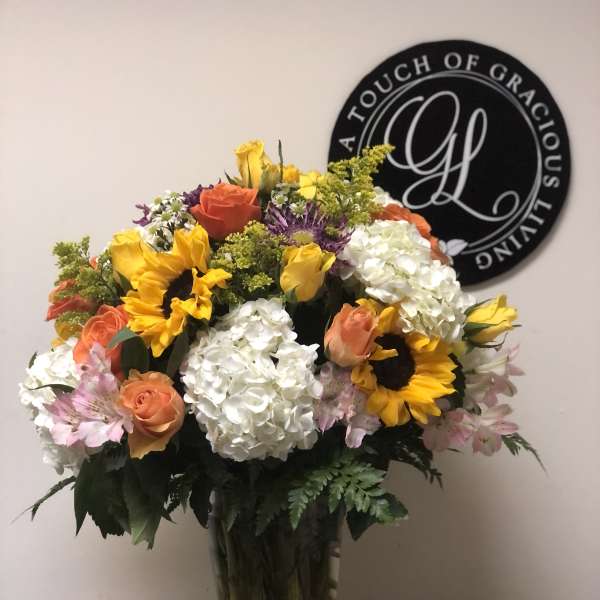 Mixed bouquet of sunflowers, roses, and white hydrangeas in a glass vase
