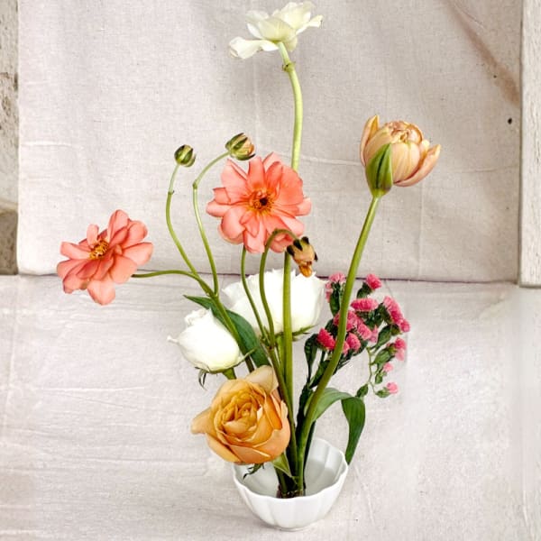 Airy arrangement of peach ranunculus, white roses, and mixed blooms in a small white ceramic bowl.