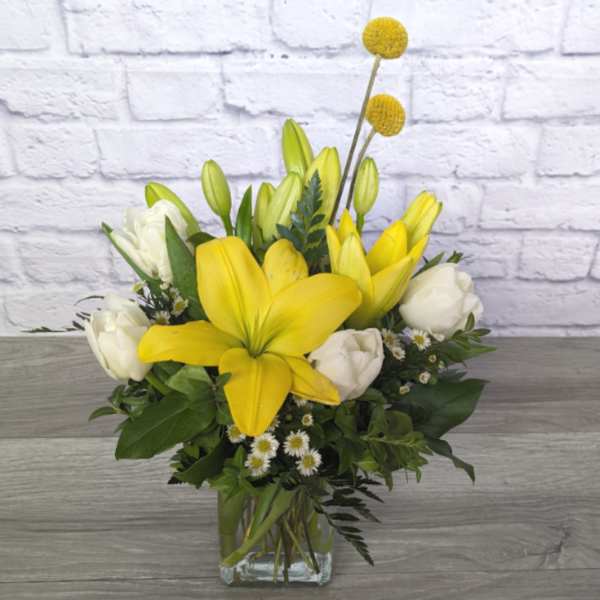Yellow lilies and white tulips in a clear glass vase