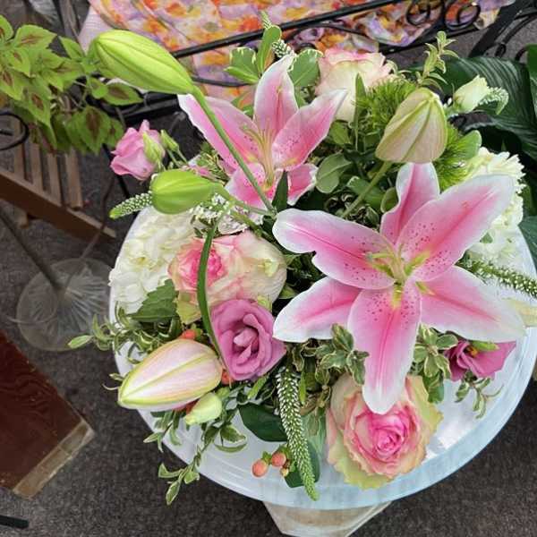 Round arrangement of pink lilies and roses mixed with white blooms in a lush bouquet.