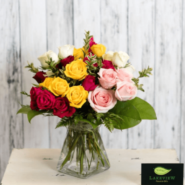 Mixed bouquet of red, yellow, white, and pink roses in a clear glass vase