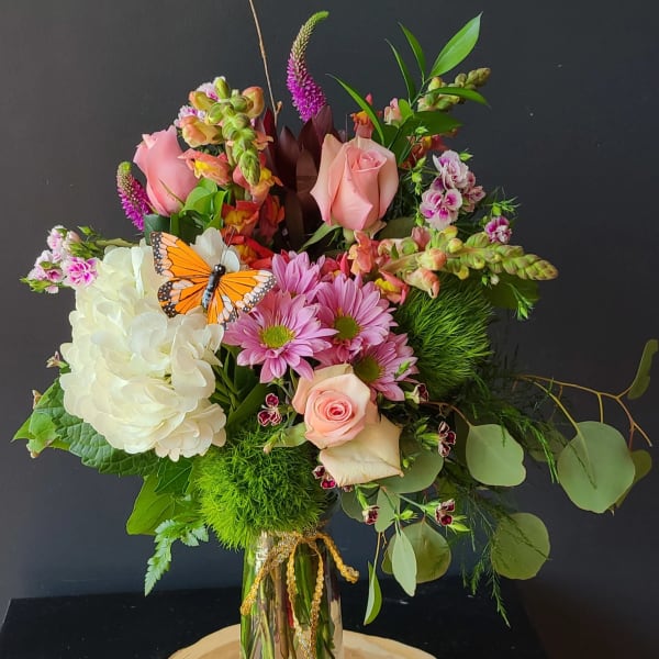 Mixed bouquet in a glass vase with pink roses, white hydrangea, and a butterfly pick