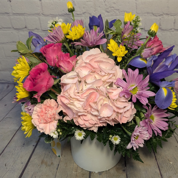 Mixed bouquet of pink, purple, yellow, and white flowers in a white vase