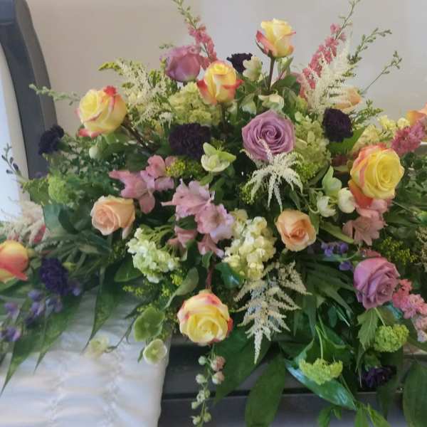 Large mixed floral spray with roses and pastel blooms on a casket