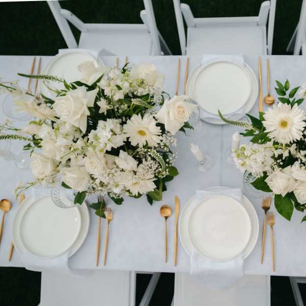White floral centerpieces on a set dining table with gold flatware