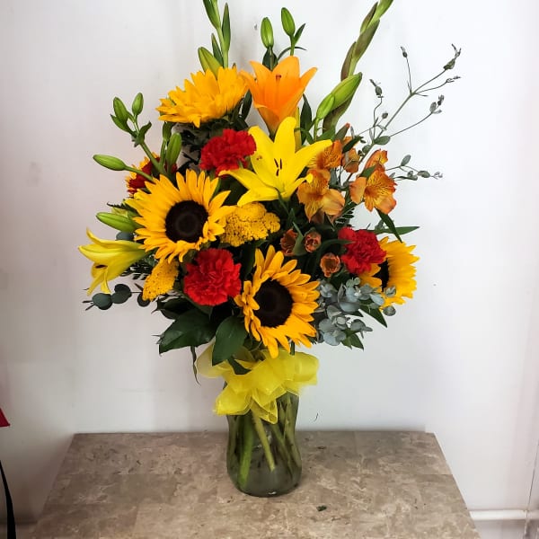 Mixed bouquet with sunflowers, lilies, carnations, and orange blooms in a glass vase