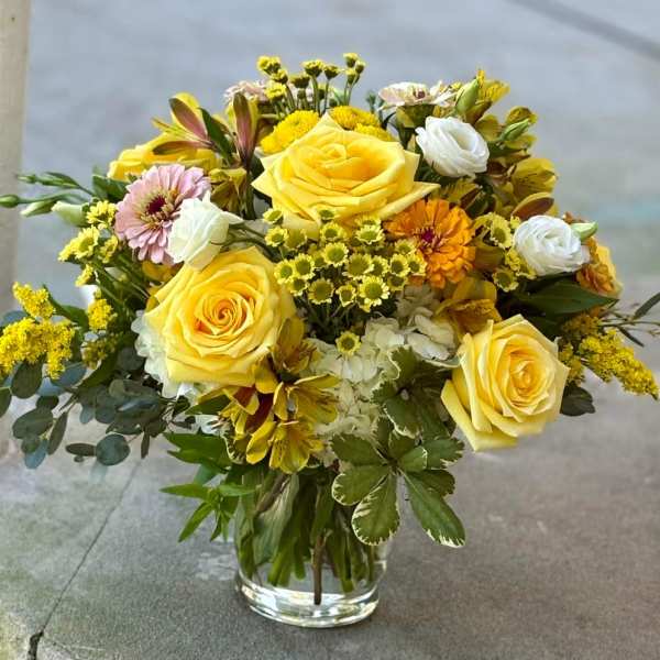 Yellow roses and mixed flowers arranged in a clear glass vase