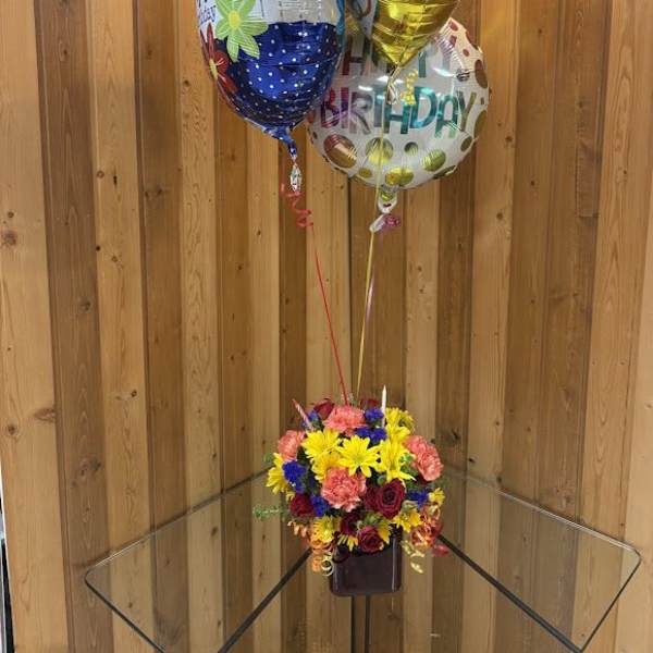 Birthday balloons above a colorful mixed flower arrangement in a vase