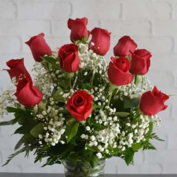 Red roses arranged in a clear glass vase with white baby's breath