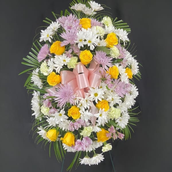 Standing floral wreath with yellow roses, white daisies, and pink ribbon