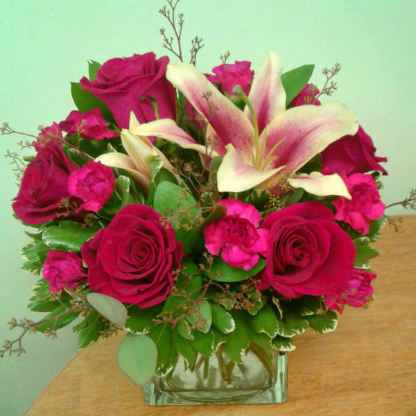 Pink roses and lilies arranged in a square glass vase