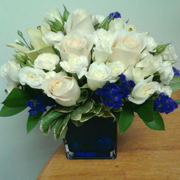 White roses and calla lilies arranged in a blue glass vase