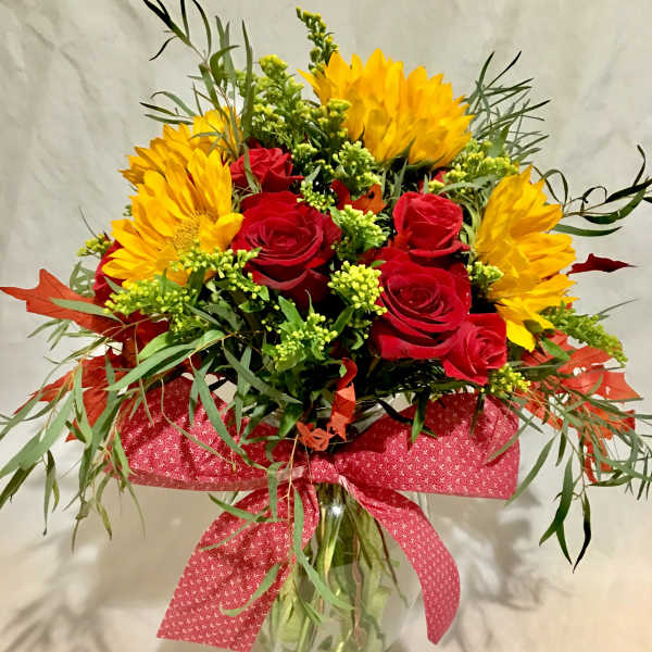 Clear vase arrangement with yellow sunflowers and red roses accented with a large red bow.