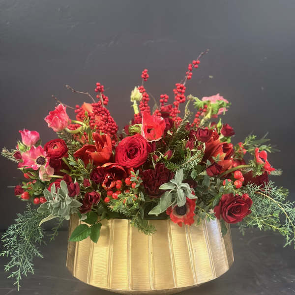 Red floral arrangement in a gold vase with berries and greenery