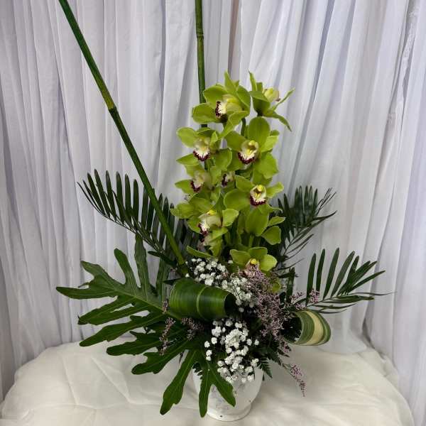 Tall green orchid arrangement in a clear vase with tropical leaves