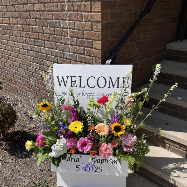 Colorful flower arrangement around a welcome sign for a baptism