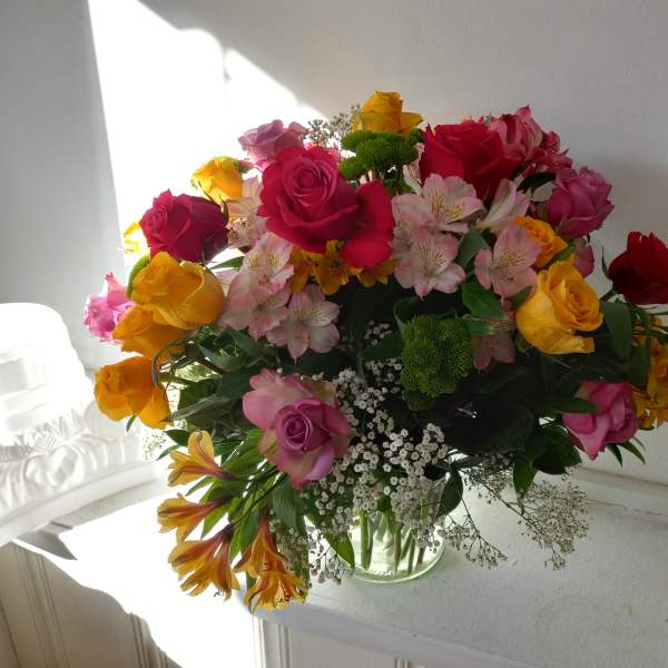 Mixed bouquet of roses, alstroemeria, and filler flowers in a glass vase