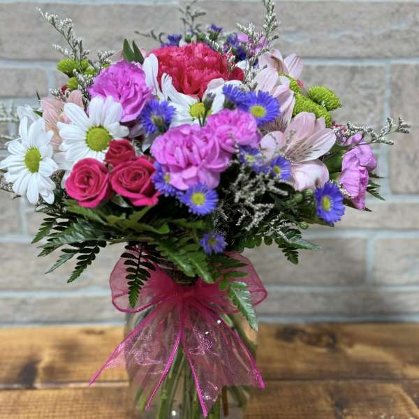 Mixed bouquet of pink, white, and purple flowers in a clear glass vase with a bright pink bow