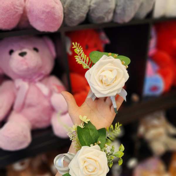 Two white rose corsages with ribbon and greenery held in a hand