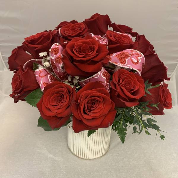 Red roses arranged in a white striped vase with pink heart decorations