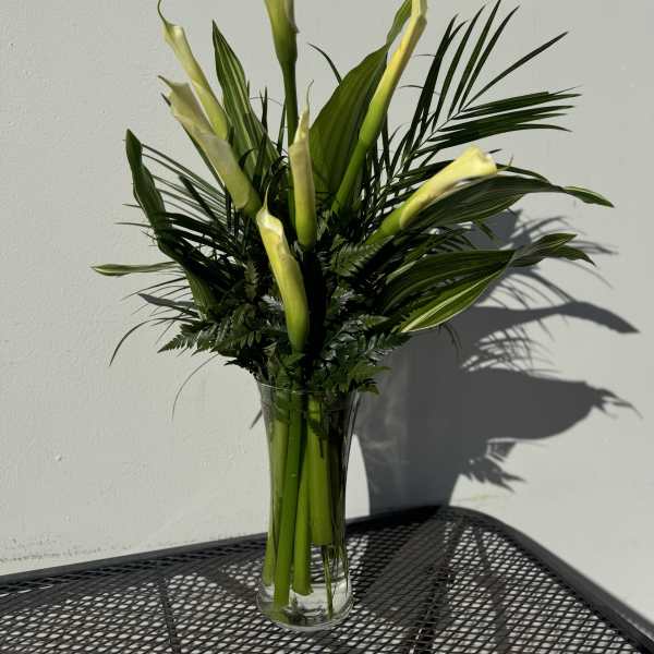 Tall arrangement of pale calla lilies in a clear glass vase