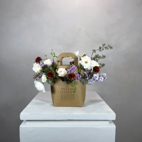 Mixed bouquet in a brown paper gift bag on a white pedestal