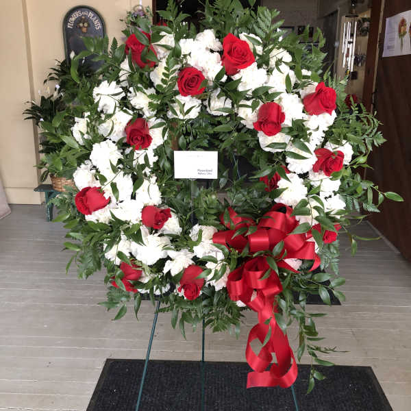 Large standing wreath of red roses and white flowers with a red ribbon