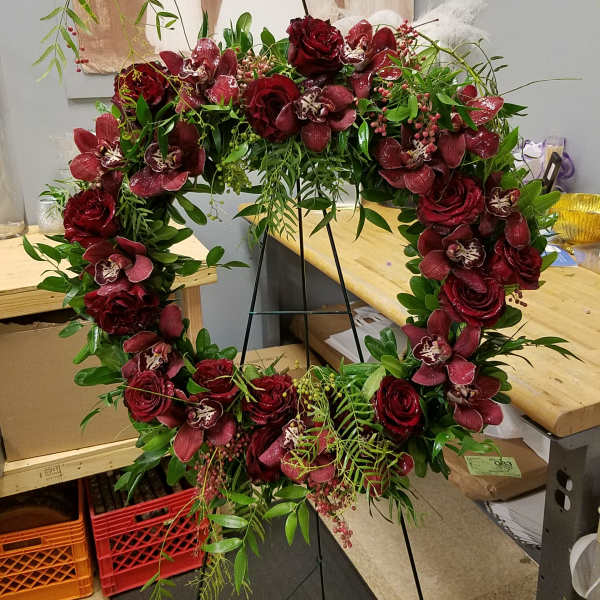 Heart-shaped floral wreath with deep red roses and orchids on a stand