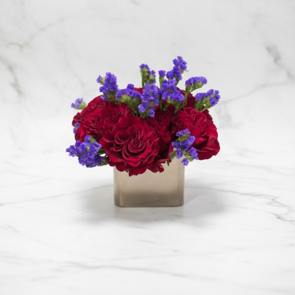Red roses and purple filler flowers in a square gold vase