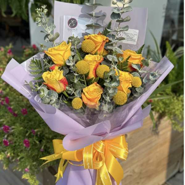 Bouquet of yellow roses with round yellow blooms wrapped in lavender paper