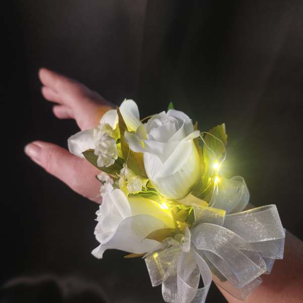 White rose wrist corsage with sheer silver bow and tiny lights on a person’s arm.