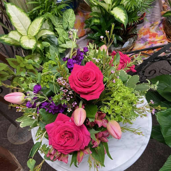 Low arrangement of hot pink roses, tulips, and mixed blooms in a white vase on a small round table