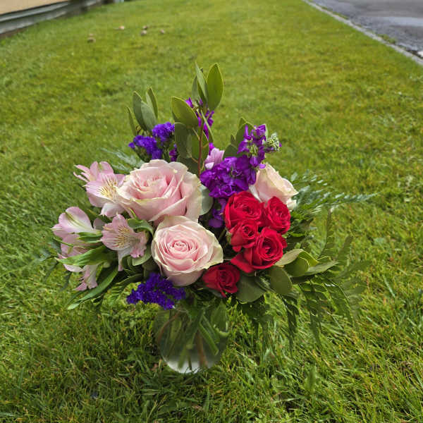 Bouquet of pink and red roses with purple accents in a glass vase